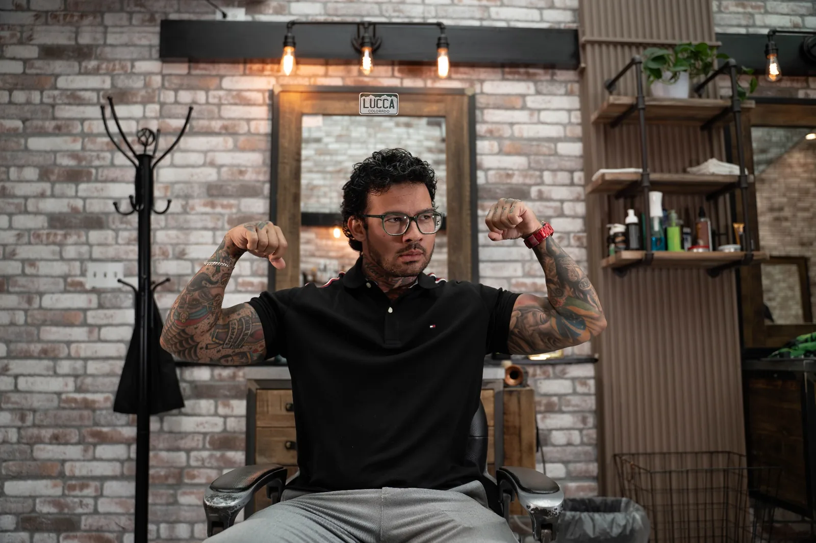 Lucca flexing his tattooed arms in the barber chair at Alfani's Barbershop on East Colfax Denver