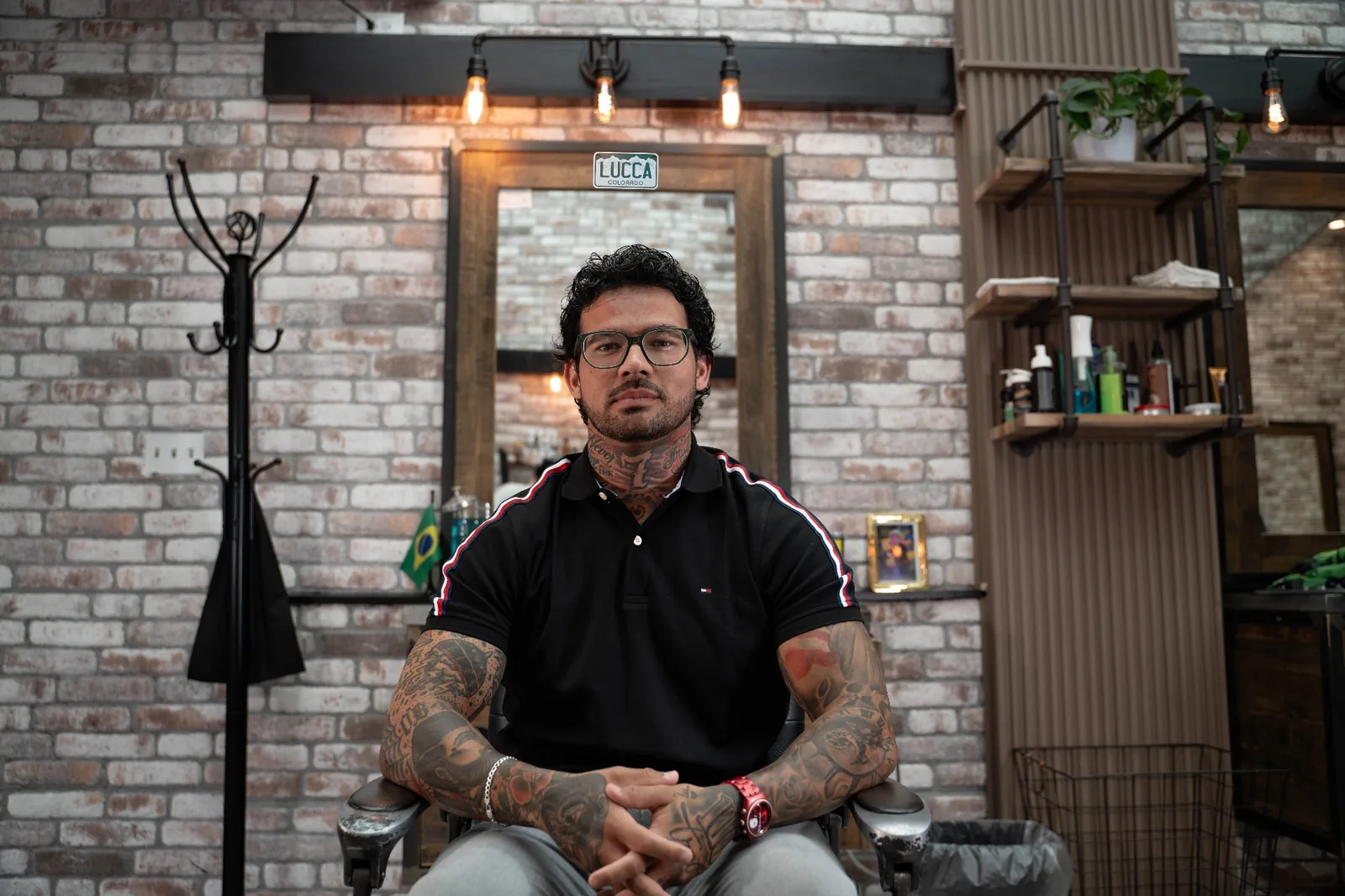 Lucca, master barber at Alfani's Barbershop Denver, seated at his station with sleeve tattoos