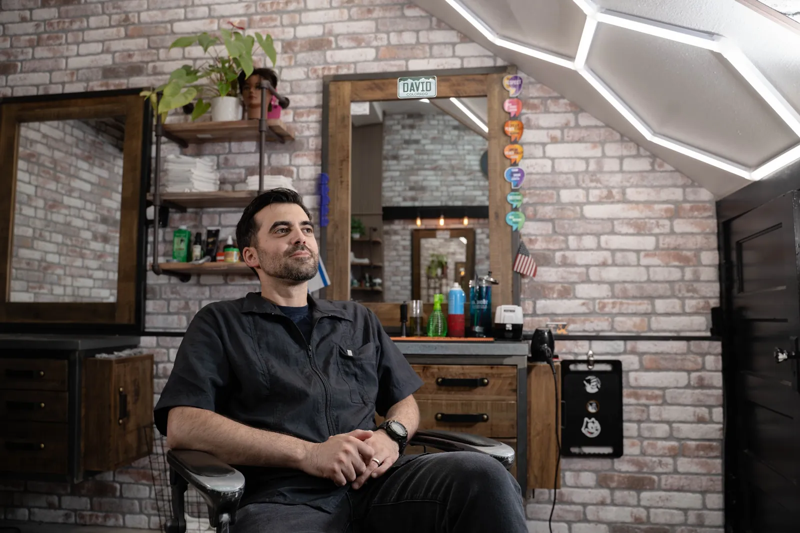 David, senior barber at Alfani's Barbershop Denver, seated at his station in a black shirt on East Colfax